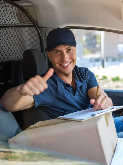 Zusteller im Lieferwagen, ein Paket auf dem Beifahrersitz, hebt lächelnd den Daumen